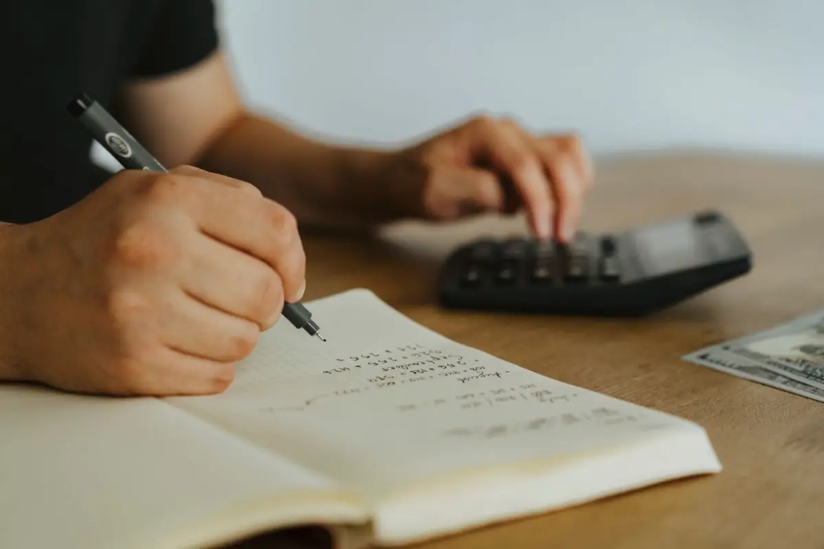 Manos que anotan cálculos en una libreta junto a una calculadora para presupuestar sesiones de terapia
