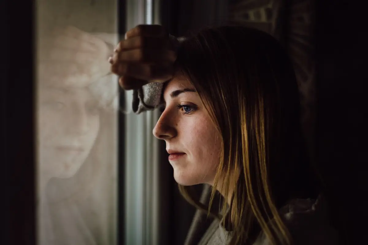Mujer pensativa apoyada en una ventana, en un momento de reflexión