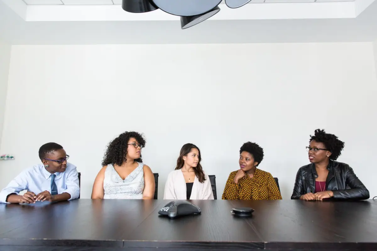 Cinco colaboradores conversan sentados en una mesa de juntas durante una reunión de trabajo