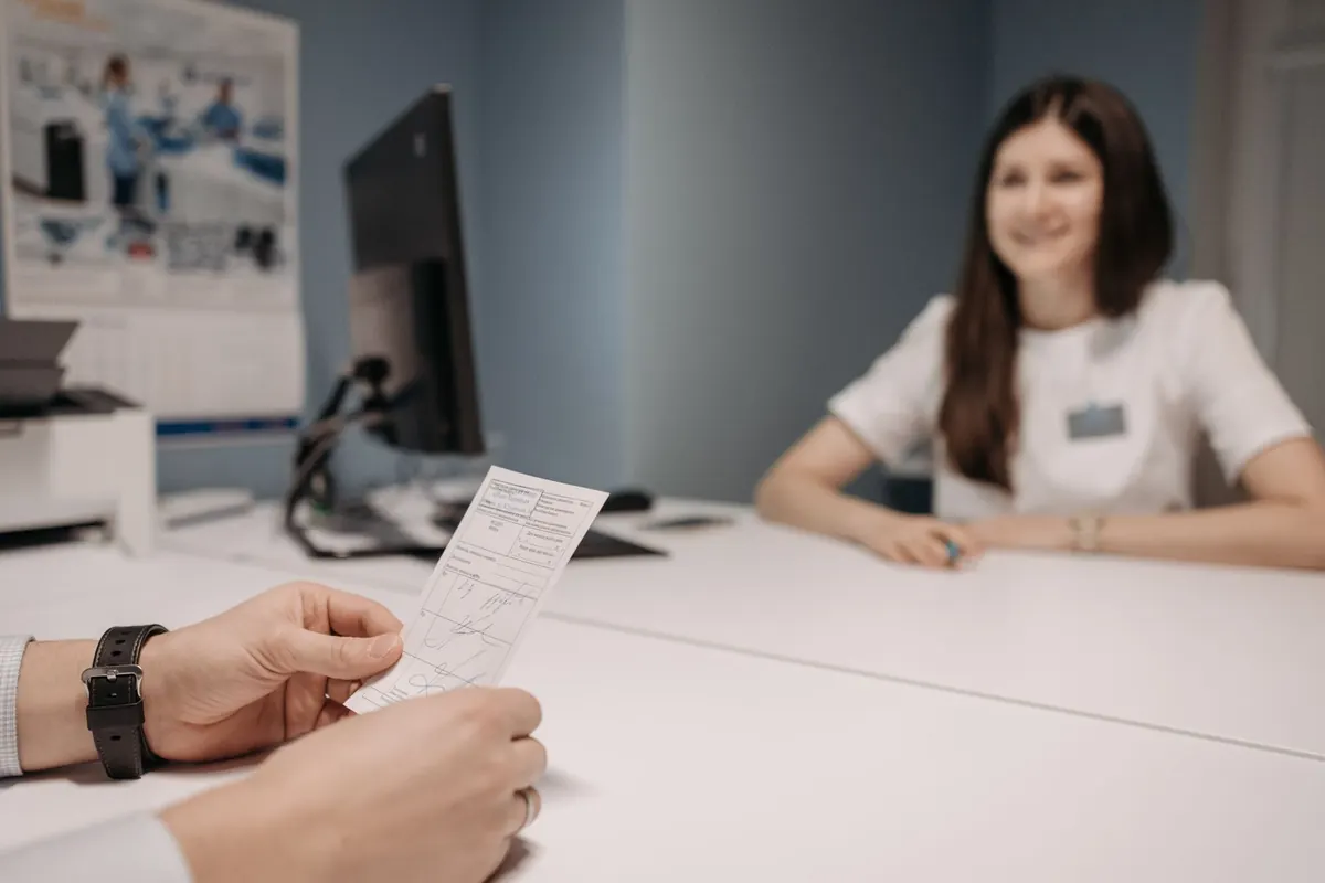 Médica en su consultorio conversa con un paciente que sostiene una fórmula médica
